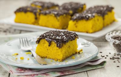 Foto de um pedaço de bolo de cenoura com cobertura de brigadeiro em um prato branco com um garfo do lado