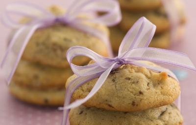 Foto com 3 cookies um em cima do outro amarrados com um cetim rosa, no fundo da foto há outros 2 cookies da mesma maneira