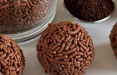 Fotografia em tons de branco com vários brigadeiros ao centro. Ao lado dos brigadeiros existe uma colher de café em pó. Fotografia em tons de branco com vários brigadeiros ao centro. Ao lado dos brigadeiros existe uma colher de café em pó.
