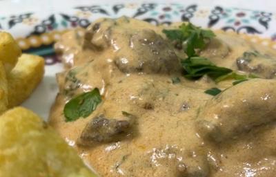 Foto da receita de Strogonoff de Carne. Observa-se um prato com o strogonoff cremoso e batatas fritas rústicas ao lado esquerdo.