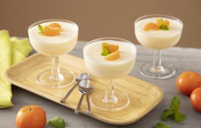 Foto da Receita de Mousse de Tangerina. Observa-se três taças de vidro com a mousse dispostas em uma tábua de madeira. Tangerinas, folhas e três colheres de sobremesa também decoram a foto