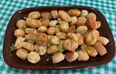 Foto aproximada da receita de pinholate de natal, bolinhas pequenas e crocantes, servidas todas em uma travessa marrom, cobertas com mel e raspas de limão