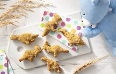 Foto da receita de Nuggets de Frango e Abobrinha. Observa-se uma tábua branca com os nuggets em formato de dinossauro sobre ela em cima de guardanapos coloridos de bolinha.