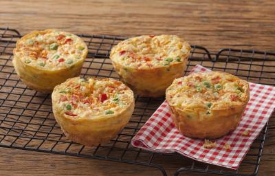 Fotografia em tons de vermelho em uma bancada de madeira com um pano xadrez vermelho com quatro muffins de tapioca com legumes.