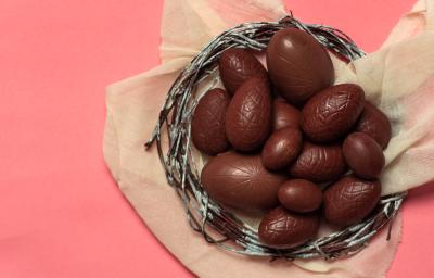 fotografia em tons de rosa e marrom de uma bancada rosa vista de cima, contém um cesto redondo com mini ovinhos de chocolate