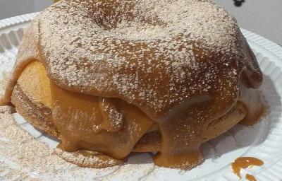 Foto em tons de marrom da receita de bolo vulcão de churros com bastante cobertura de doce de leite com canela salpicada por cima