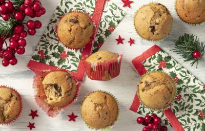 Foto da Receita de Muffin Natalino feito na Air Fryer. Observa-se 7 muffins de baunilha com chocolate em forminhas natalinas vistos de cima. Decorações natalinas enfeitam a foto, como guardanapos e decorações de árvore de Natal.