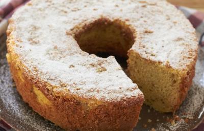 em uma mesa de madeira contém um pano xadrez nos tons vinho e cinza e por cima do pano o bolo de fubá coberto com açúcar de confeiteiro.