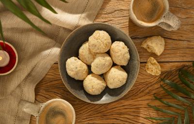 Foto da receita de pão de queijo de aveia servida em diversas porções em um bowl de cerâmica cinza em cima de uma mesa de madeira com um pano de linho ao lado