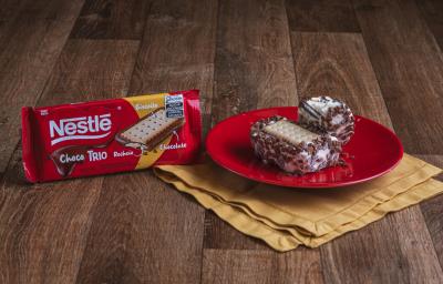 Foto da Receita de Sanduíche de Sorvete com Choco Trio. Observa-se dois sanduíches (um inteiro e um mordido) sobre um prato vermelho redondo e pequeno e, ao lado, a embalagem de ChocoTrio