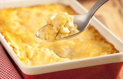 fotografia em tons de marrom, vermelho, amarelo e branco tirada de uma tábua de madeira, por cima um recipiente retangular vermelho e branco com a batata gratinada dentro.