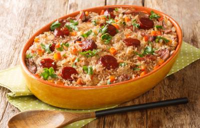 Fotografia mostra um arroz com pedaços de linguiça e temperos verdes dentro de uma travessa de servir.