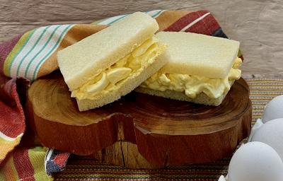 Foto da receita de Sanduíche de Ovos. Observa-se uma tábua de madeira com dois sanduíches de pão de forma sem casca com o recheio de ovos dentro sobre a tábua.