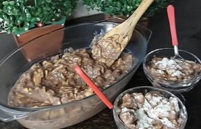 Foto da receita de brigadeirão crocante servida em uma porção grande e em duas taças de vidro com colheres vermelhas, tudo isso sobre uma mesa preta