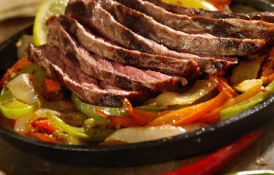 Fotografia de tirinhas de carne com cebola e pimentão temperadas. As carnes estão por cima dos legumes, que estão dentro de uma panela de ferro.