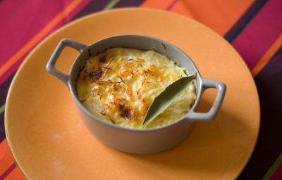 Fotografia de um recipiente pequeno que foi ao forno com uma receita de chuchu recheado com creme de milho e frango. A receita foi gratinada e tem uma folha de louro por cima.