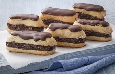 Fotografia em tons de azul em uma mesa de madeira azul com um paninho azul e por cima um guardanapo branco de papel e seis bombas de chocolate com cobertura de chocolate em cima.