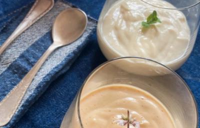 Foto da Receita de Mousse Clássico de Pitanga e Cupuaçu. Observa-se duas taças de vidro transparentes com a mousse sobre um jogo americano azul marinho e duas colheres ao lado, em um guardanapo de pano listrado.