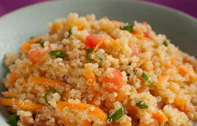 Fotografia em tons de laranja de uma bancada roxa com um prato fundo cinza com a salada de quinoa, tomate, cenoura ralada e cebolinha.