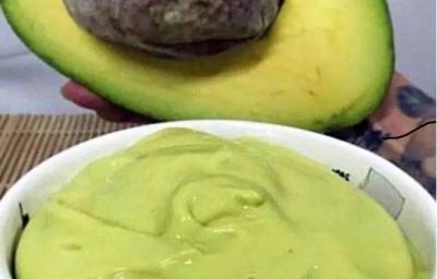 Foto da receita de Mousse de Abacate. Observa-se um potinho branco com a mousse cremosa dentro e um abacate pela metade atrás ilustrando.