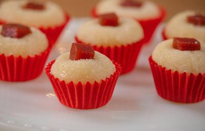 Fotografia de sete unidades de forminhas vermelhas com brigadeiro de romeu e julieta. Por cima de cada um tem um quadradinho de goiabada, e todos estão sobre um apoio decorativo de cor branca.