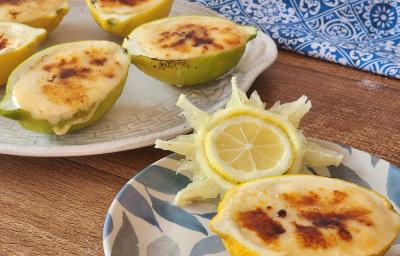 Foto em tons de amarelo da receita de limão brullée servida em três porções divididas em dois pratos decorados sobre uma mesa de madeira com um pano azul ao fundo