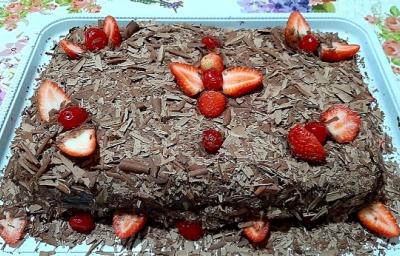 Foto em tons de marrom da receita de bolo de chocolate com morangos servida inteira e decorada com morangos e cerejas em cima