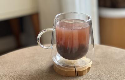 Foto da receita de Bubble Tea Caseiro, servido em uma xícara de vidro transparente, sobre uma pequena base de madeira em uma mesa