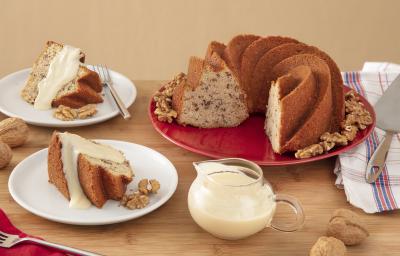 Foto da Receita de Bolo de Nozes com Molho doce. Observa-se dois pratos de sobremesa com pedaços do bolo e a calda. Ao lado direito, um prato redondo vermelho grande com o restante do bolo, decorado por nozes.