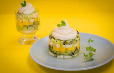 fotografia em tons de amarelo e branco, contém um prato redondo e branco com Tartar com pedaços de frutas e creme por cima e ao fundo uma taça transparente com pedaços de frutas e creme por cima.