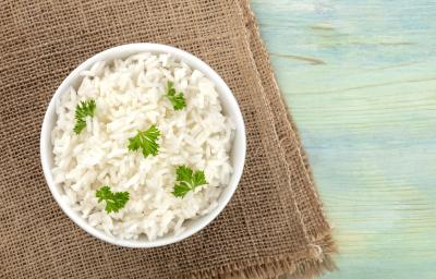 fotografia em tons de azul, marrom e branco de uma bancada azul vista de cima. Contém um pano marrom ao lado esquerdo, por cima um recipiente redondo branco com arroz e salsa.