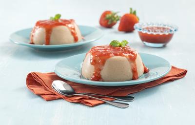 Foto da receita coringa de Flan. Observa-se dois pratos azuis claros com o flan e a calda de morangos por cima, o da frente sobre um guardanapo marrom e ao lado duas colheres de sobremesa. Ao fundo, morangos e a calda em um pote decoram o cenário.