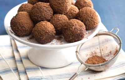 Fotografia em tons de azul em uma bancada de madeira azul clara, um pano branco listrado, um suporte branco com várias trufas de iogurte com chocolate.