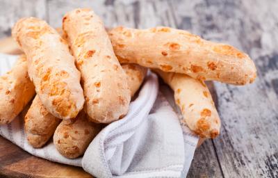 Fotografia em tons de cinza com uma toalha branca ao centro. Em cima da toalha existe vários biscoitinhos de polvilho dourados.