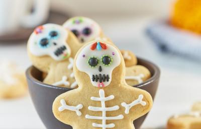 Imagem aproximada de um biscoito em formato de caveira com a decoração no tema de halloween, em uma bancada em tons claros