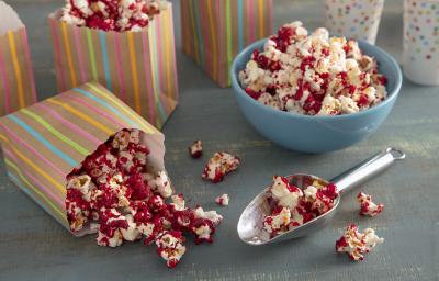 Foto da receita pipoca doce vermelha. Observa-se uma tigela azul com a pipoca e, ao lado, saquinhos estampados com a pipoca também.