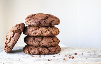 fotografia em tons de branco e marrom de uma bancada branca vista de frente. Contém 4 cookies de chocolate empilhados e um ao lado.