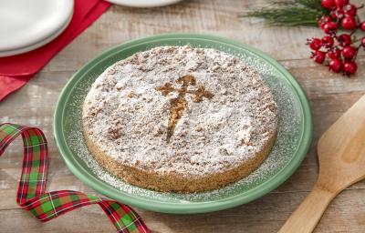 Foto da receita de torta de santiago servida em um prato verde grande sobre uma mesa de madeira com decoração de natal e uma espátula de madeira ao lado