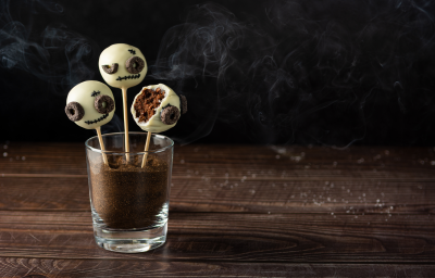 Fotografia de um bolo no palito coberto por chocolate branco, decorados com carinhas de monstro.