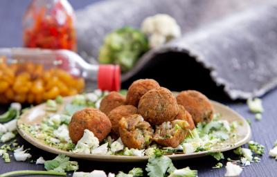 Foto da receita de bolinho de talos, servido em um prato sobre uma bancada cinza com garrafas de pimenta ao fundo