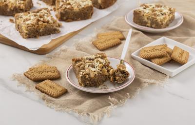 Foto da receita de Blondie de Tostines. Observa-se um prato de sobremesa com uma fatia de blondie com uma colher retirando uma fatia. Biscoitos TOSTINES decoram a foto.