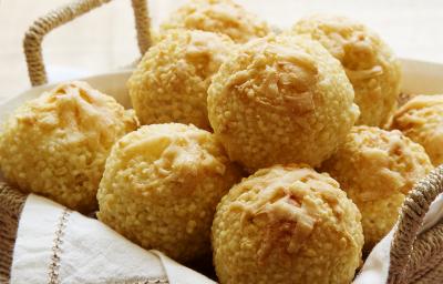 Fotografia em tons de marrom em uma bancada de madeira com uma cestinha de vime com vários pãezinhos de tapioca redondos dentro.