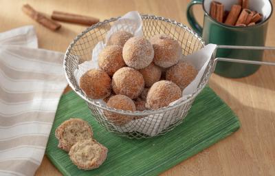 Foto da receita de bolinho de chuva sem glúten. Observa-se uma peneira com os bolinhos dentro, polvilhados de açúcar e canela, sobre um guardanapo de pano verde