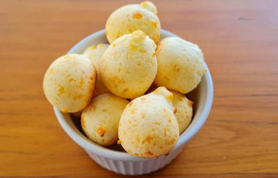 Fotografia de um ramekin branco com vários pães de queijo. O recipiente está sobre uma mesa de madeira.