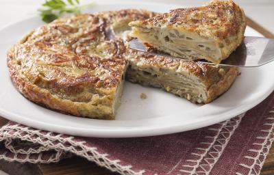 Fotografia em tons de marrom em uma bancada de madeira com um jogo americano vinho com um prato raso branco com a omelete recheada em cima dele.