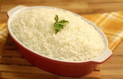 Foto de um recipiente vermelho com arroz branco dentro e uma folha de coentro decorando