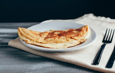 Foto aproximada da receita de Crepioca de Aveia em Flocos, em um prato branco, sobre um tecido em tom bege, com dois talheres de metal ao lado.