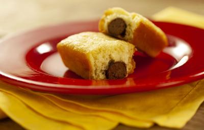 Fotografia em tons de vermelho e amarelo de uma bancada de madeira com um paninho amarelo e sobre ele um prato vermelho com dois mini bolinhos recheados com um baton.