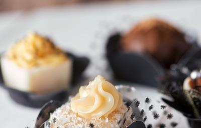 Fotografia de alguns docinhos de banana decorados. Ao fundo, docinhos de chocolate também decorados, sobre uma mesa de madeira em tom claro.