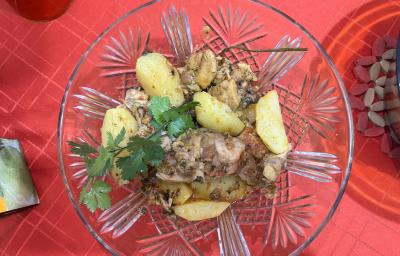 Fotografia vista de cima de um recipiente fundo de vidro com frango cozido, batatas e coentro por cima. O recipiente está sobre uma toalha de mesa vermelha.